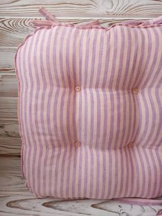 a pink and white striped pillow sitting on top of a wooden floor next to a wall