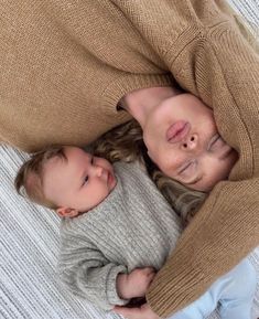 a woman holding a baby in her arms while laying on top of a white blanket