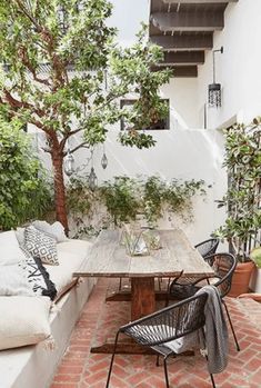 an outdoor dining area with brick flooring and wooden table surrounded by potted plants