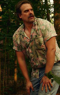 a man holding a frisbee in his right hand while standing next to trees