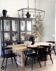 a dining room table with black chairs and a glass case on the wall behind it