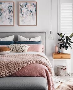 a bed with pink and grey sheets in a bedroom next to two pictures on the wall