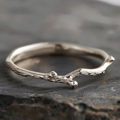 a silver ring sitting on top of a rock with a small branch in the middle