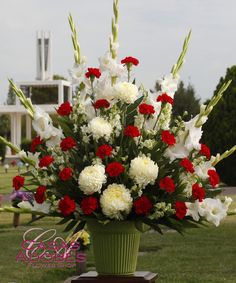 This arrangement is a beautiful way to celebrate the life of your loved one. It is made with red carnations, white football chrysanthemums, white larkspur, white gladiolas and lush foliage. Altar Flowers Floor, Church Nativity Flowers Arr@ngement, Large Flower Arrangements For Church Wedding, 50 Th Anniversary Flower Arrangements, Christmas Flower Arrangements For Church Wedding Centerpieces, Catholic Church Wedding Flowers Altar, Large Flower Arrangements For Church Pedestal, Church Flower Arrangement Year Round, Chrysanthemum Flower Arrangement