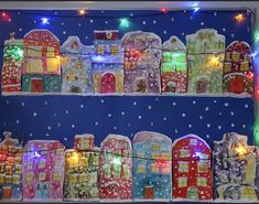 a christmas display with lights and houses in the snow on blue background, decorated with multicolored garlands