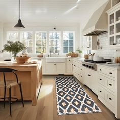 a large kitchen with white cabinets and wooden flooring, along with an area rug