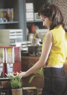 a woman standing in front of a laptop computer next to a potted plant on top of a table