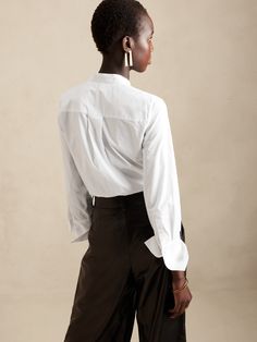 A seamless silhouette, this soft tuxedo shirt is made from 100% cotton with a concealed button front, elegant pintuck detail and exaggerated cuffs.  SEMI-FITTED: Cut for a not-too-tight, not-too-loose fit.  Banded collar.  Hidden button front.  Troca Modern Workwear Tops With Concealed Placket, Modern Tops With Concealed Placket For Workwear, Modern Tops For Workwear With Concealed Placket, Chic Business Casual Tops With Spread Collar, Chic Office Tops With Hidden Button Closure, Timeless Button-up Office Tops, Timeless Tailored Tops For Office, Timeless Long Sleeve Tops With Concealed Placket, Fitted Tops With Placket And Shirttail Hem