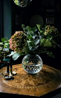 a glass vase filled with flowers sitting on top of a table next to a mirror ball