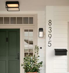 a green front door on a white house with potted plant and mailbox next to it