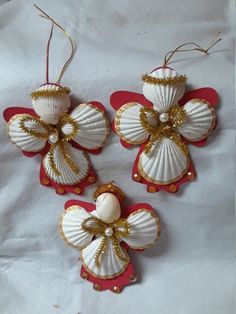 three seashell ornaments are hanging from red and white ribbons on a white tablecloth