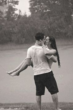 a man carrying a woman on his back while standing in the rain near a body of water