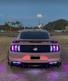 the front end of a pink mustang in a parking lot with purple lights on it