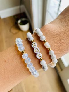 two bracelets with white beads and gold letters on the wrist, one is personalized