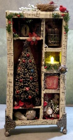 a small christmas tree in a wooden cabinet with ornaments around it and a lit candle