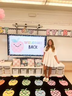 a woman standing in front of a welcome back sign with apples on the floor and pink pom poms