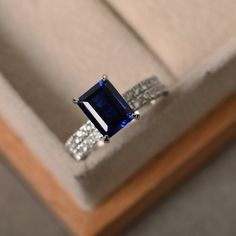 an engagement ring with a blue stone surrounded by white diamonds in a wooden box on display