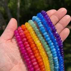 a hand holding five different colored beads in it's palm, with trees in the background