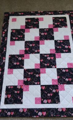 a black and pink quilted with hearts on it's side, sitting on the floor