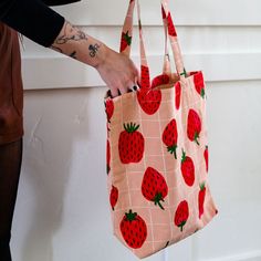 a woman is holding a bag with strawberries on it and has tattoos on her arm