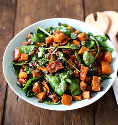 a white bowl filled with spinach and sweet potato salad on top of a wooden table