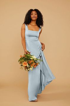 a woman in a long blue dress holding a flower bouquet and looking at the camera