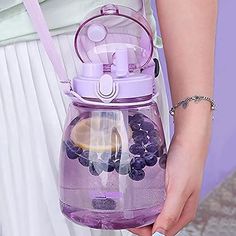 a woman is holding a purple water bottle with fruit inside and attached to the handle