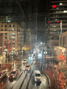 cars are driving down the street in the rain at night with buildings and traffic lights