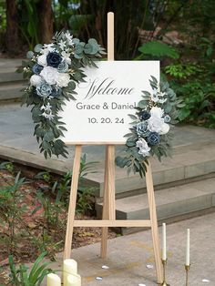 a wedding sign with flowers and greenery on the ground in front of some candles