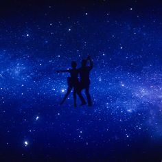 two people are standing in the air with their arms around each other and looking up at the stars