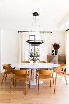 a dining room table with four chairs and a vase on the top of it in front of a window