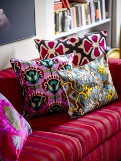 colorful pillows on a red couch in front of a bookshelf and bookcase