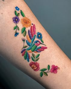 a woman's arm with colorful flowers and leaves tattooed on the left side of her leg