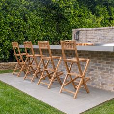 four wooden chairs sitting on top of a cement slab in front of a brick wall