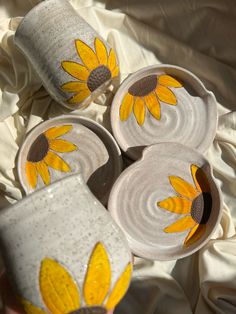 three yellow sunflowers painted on white pottery cups and saucers sitting on a bed