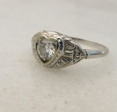 an antique style ring with a heart shaped diamond in the center on a white surface