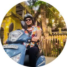 a man riding on the back of a blue scooter in front of a yellow house