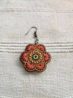 a pair of earrings with an orange and green flower design on the front, sitting on top of a white cloth