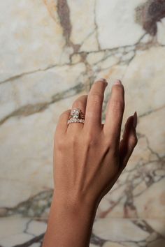 a woman's hand with a diamond ring on her left hand, against a marble background