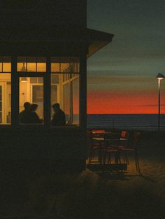 two people sitting at a table in front of a window with the sun setting behind them