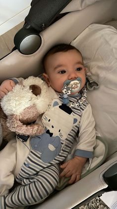 a baby laying in a stroller with a stuffed animal and pacifier to his mouth