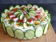 a cake with cucumbers and ham on it sitting on a wooden cutting board