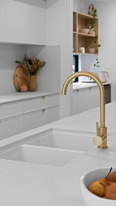 a kitchen with white counter tops and gold faucet