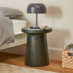 a small table with a lamp on it next to a bed