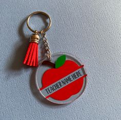 an apple shaped keychain with a tasseled name tag attached to it