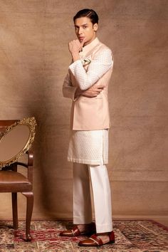 Soft pink bundi in italian polywool with button placket. Paired with white checkered kurta and trouser.
Components: 3
Neckline: Band collar
Sleeve Type: Bundi: Sleeveless, Kurta: Full
Fabric: Bundi: Italian polywool, Trouser: Cotton silk, Kurta: Self chanderi
Color: Pink, White
Other Details: 
Button placket
Side slits
Note: The pocket squares worn by the model is not for sale
Occasion: Mehendi and Puja - Aza Fashions Elegant Nehru Jacket With Button Closure For Festive Season, Festive Nehru Jacket With Button Closure For Semi-formal Occasions, Festive Nehru Jacket For Semi-formal Occasions, Festive Nehru Jacket With Buttons, Designer Nehru Jacket For Semi-formal Occasions, Festive Semi-formal Nehru Jacket With Button Closure, Kurta Set Men, Sleeveless Kurta, Kurta Set For Men