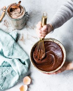 a person holding a whisk in a bowl with chocolate frosting on it