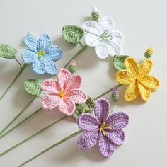 crocheted flowers are arranged on a white surface with green stems and yellow centers