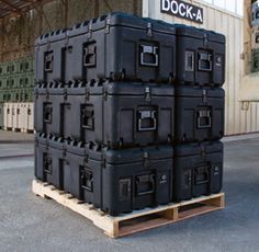 large stack of black suitcases sitting on pallets in front of a warehouse building