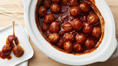 meatballs with sauce in a white crock pot on a wooden table next to small plates